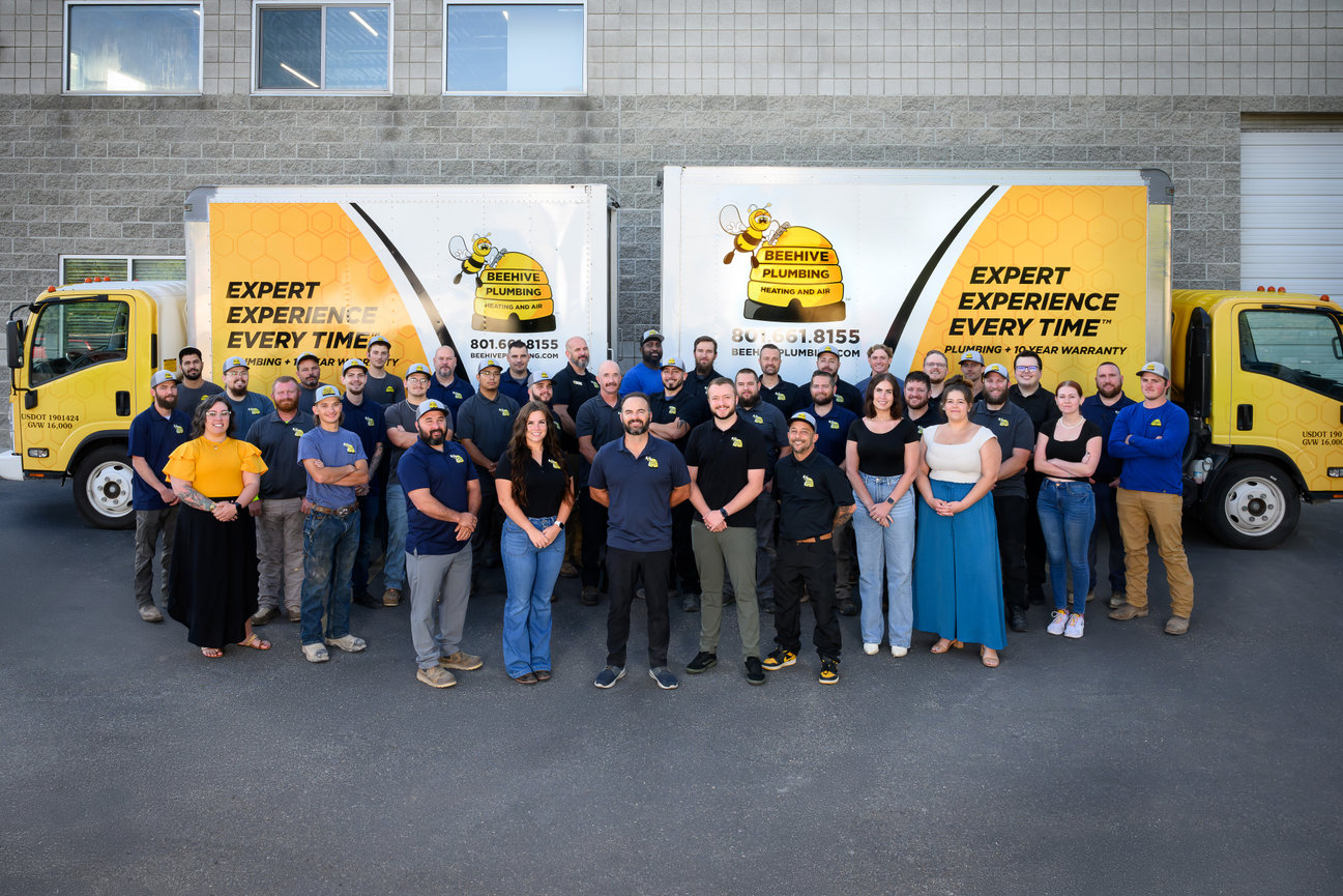 Group photo of the BeeHive Plumbing team in front of two branded trucks.