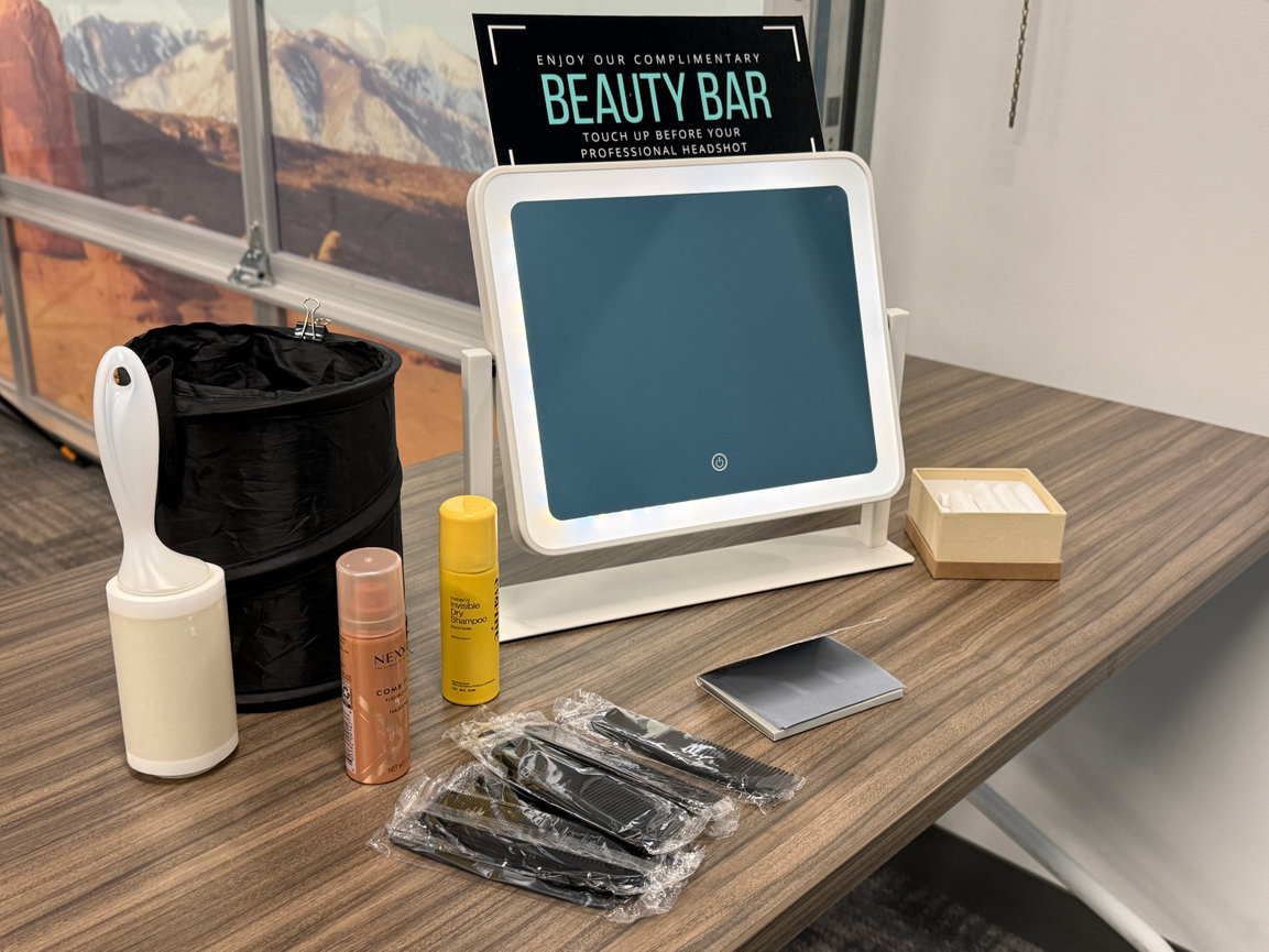 Beauty bar setup with a mirror, lint roller, spray, combs, wipes, and box on a wooden table.
