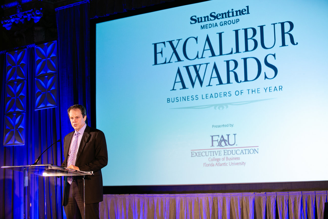 Man speaking at a podium during the Sun Sentinel Excalibur Awards business event.