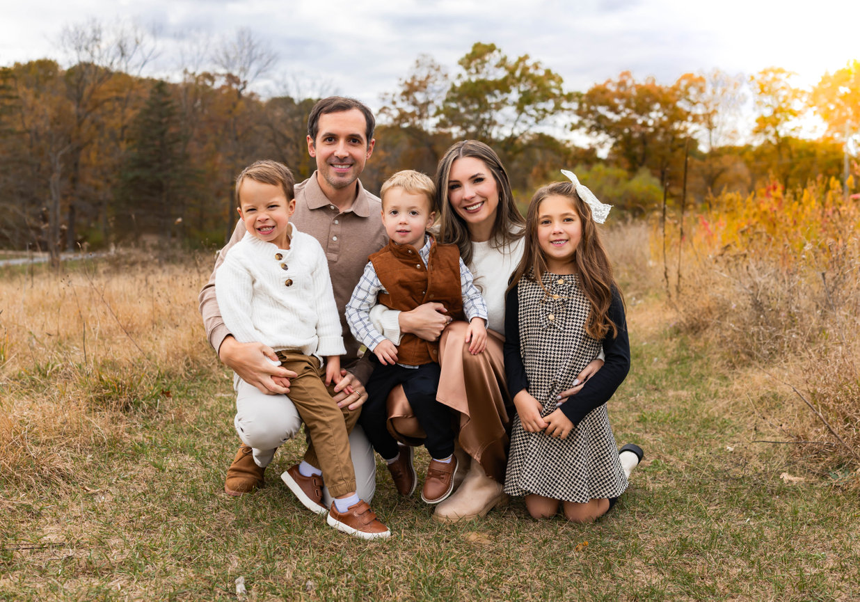Family of three with baby seated on blanket during outdoor session in Farmington, MI