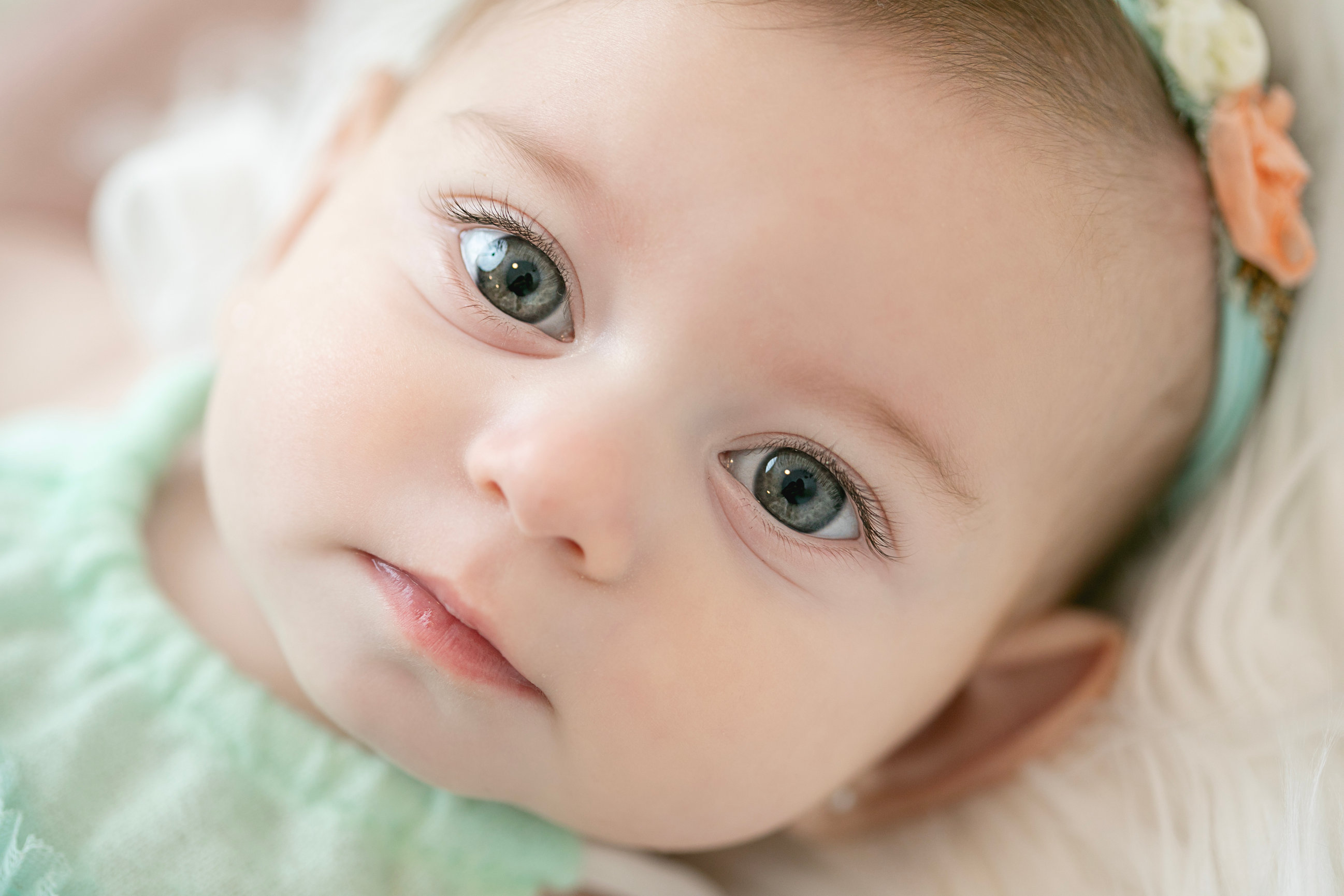 Close portrait of a baby wearing a mint green outfit and floral headband