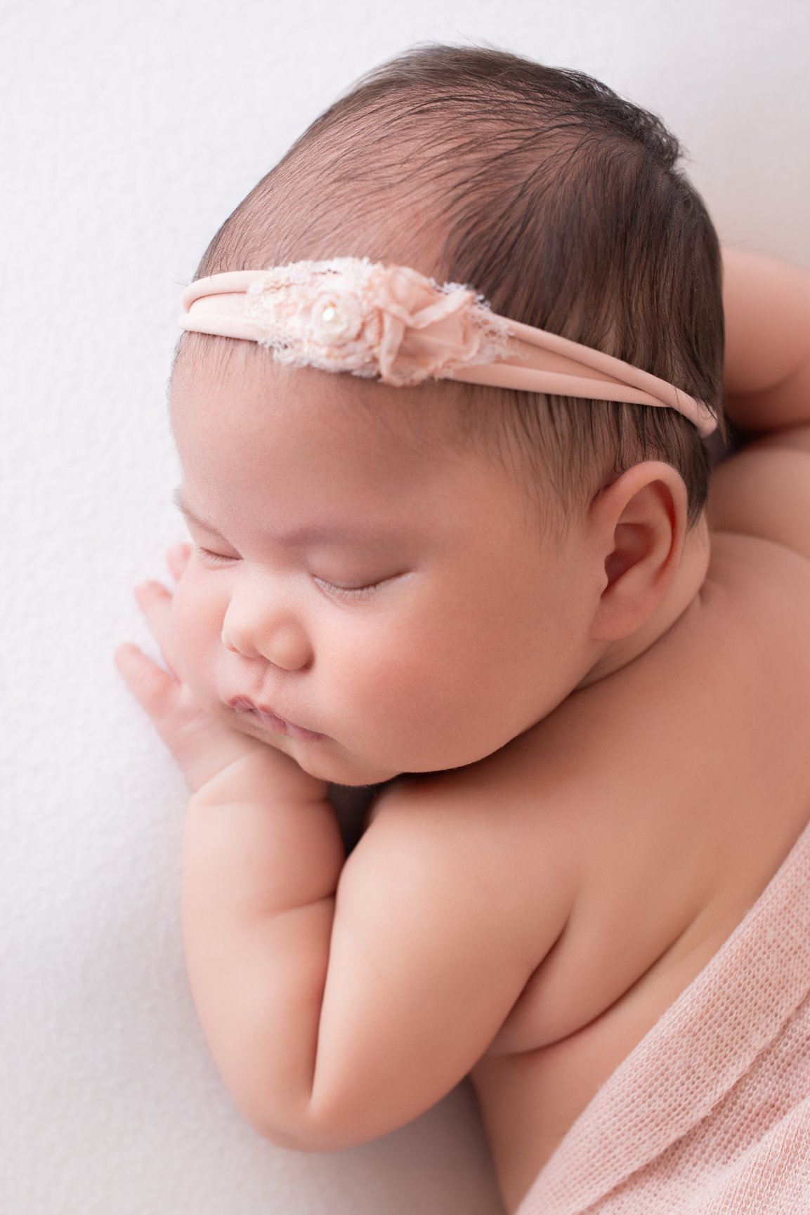 Close-up of a sleeping newborn girl in profile with a lace headband