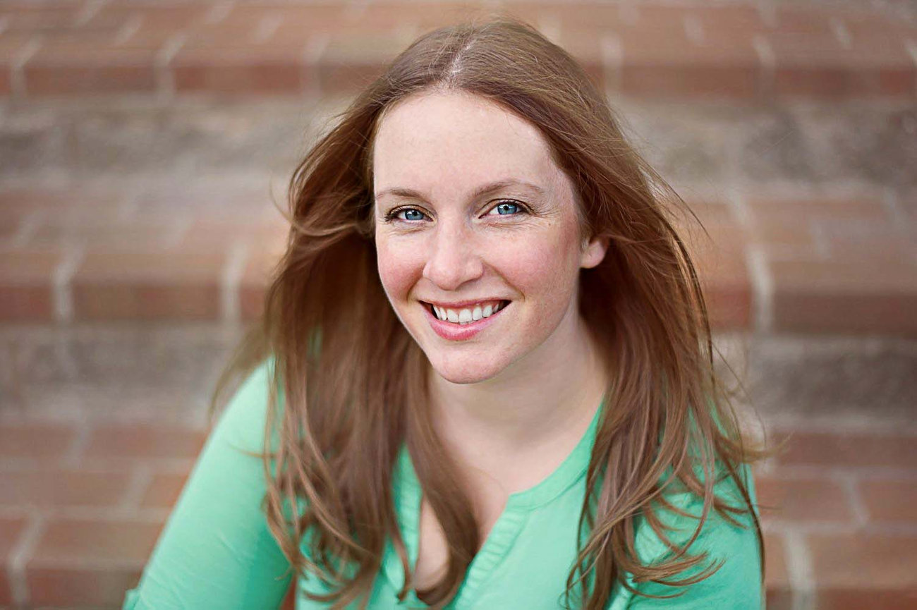 A smiling person with long brown hair and a green shirt sits on brick steps, capturing the perfect graduation photography moment.