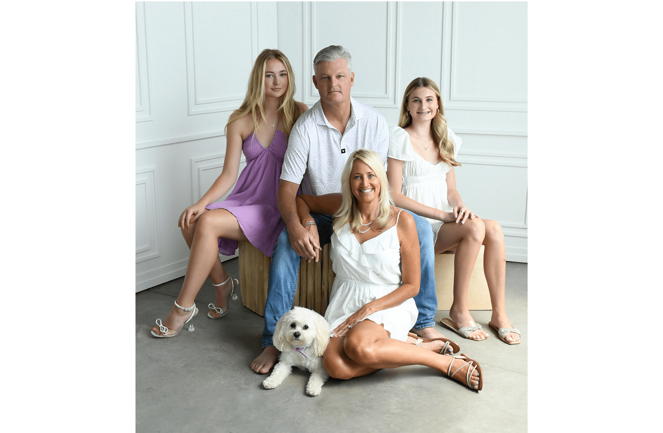 Mom and dad and their high school ages daughters in spring dresses with their white fluffy dog.