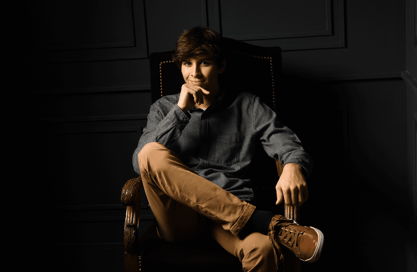 A high school senior in khaki pants poses pensively.