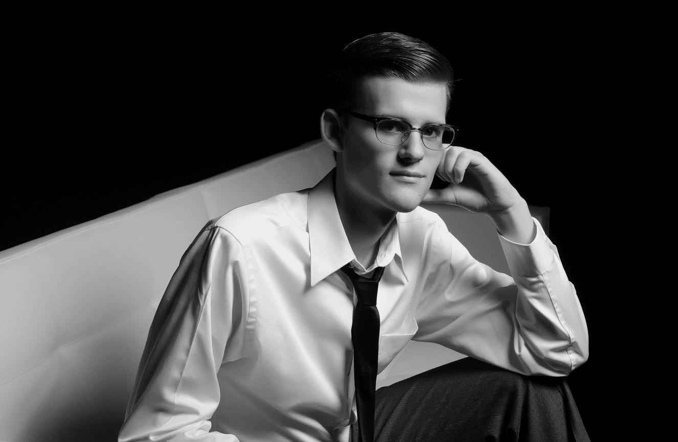 A teenager wearing a white button down and black tie looking thoughtful.