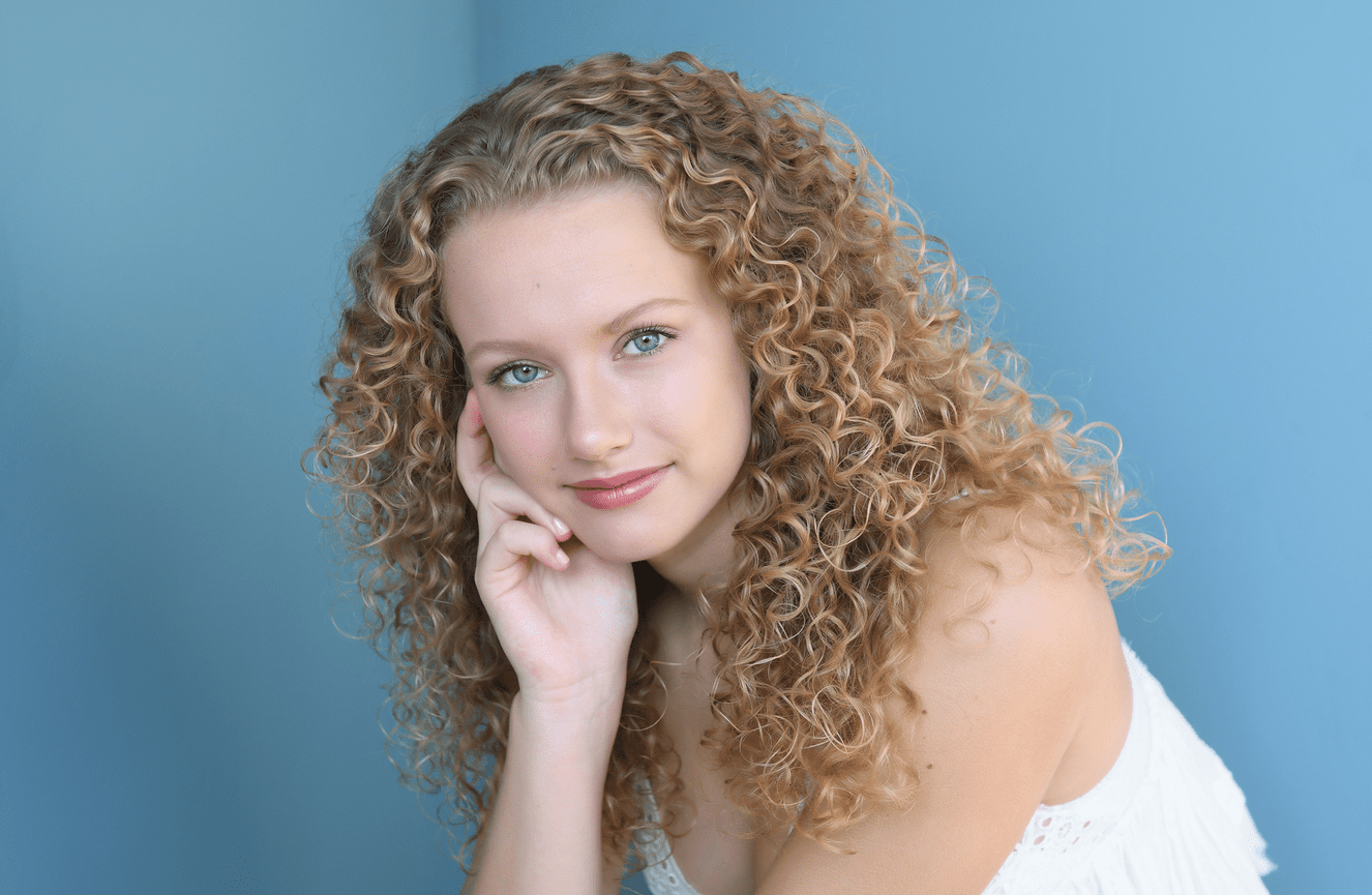 A teenage girl with a mop of spiral blonde curls against a vibrant blue background.
