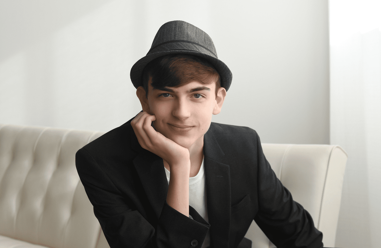 A young man looking comfortable wearing a suit jacket and fedora.