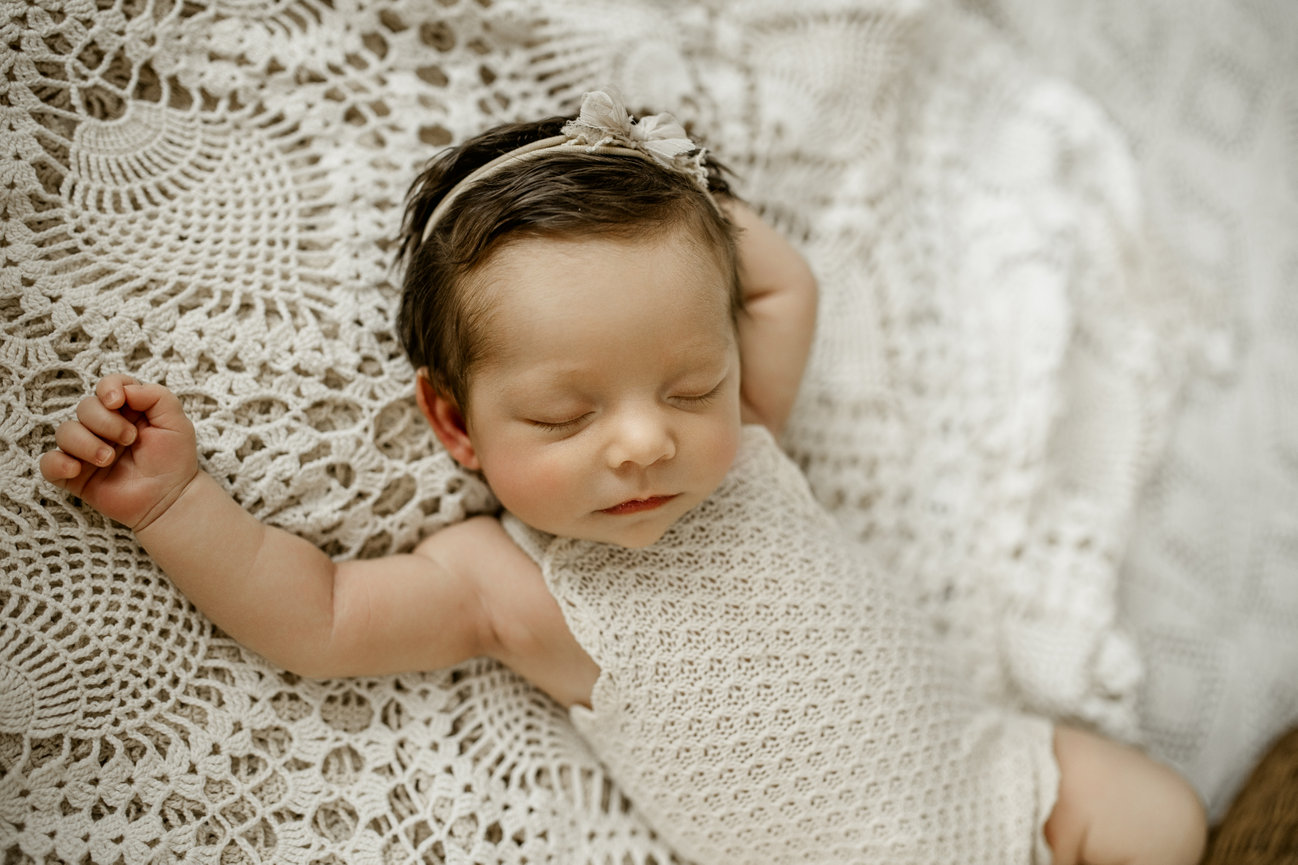 Sleeping baby swaddled in a knitted outfit on a textured cream blanket.