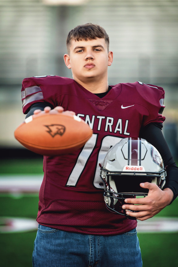 Westosha Central High School football player in maroon jersey holding a football and helmet on a field for his senior pictures.