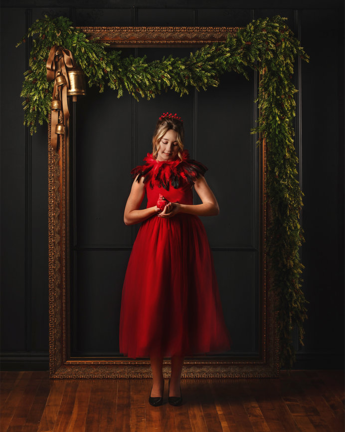 Woman in a red gown standing in a dark framed floral portrait setup