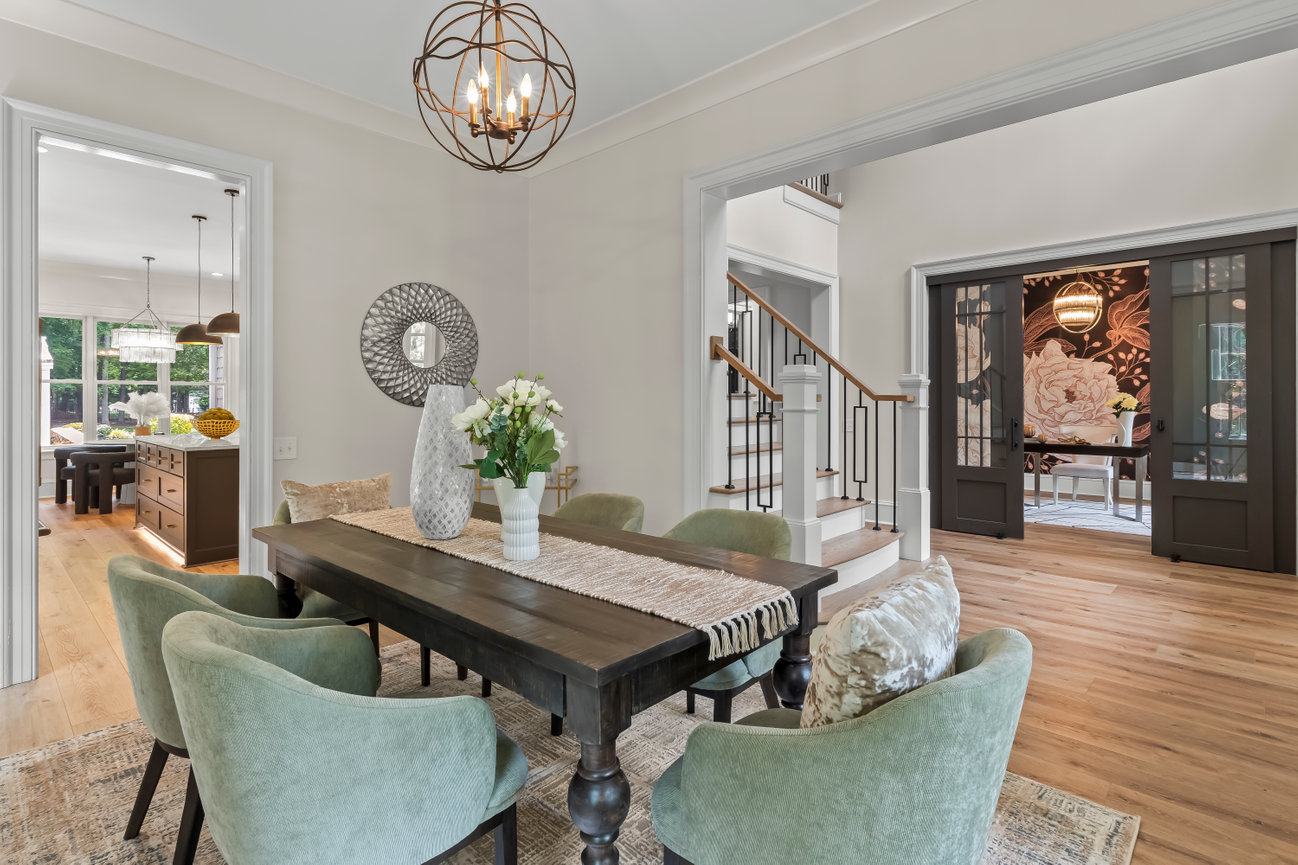 Modern dining room with dark wood table, green chairs, chandelier, and open view to staircase and adjacent rooms