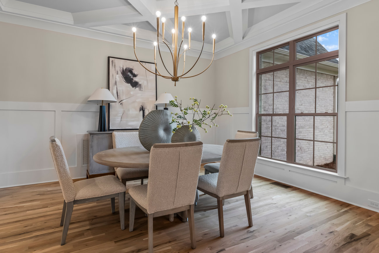 Elegant dining room with round table, upholstered chairs, modern chandelier, and large window.