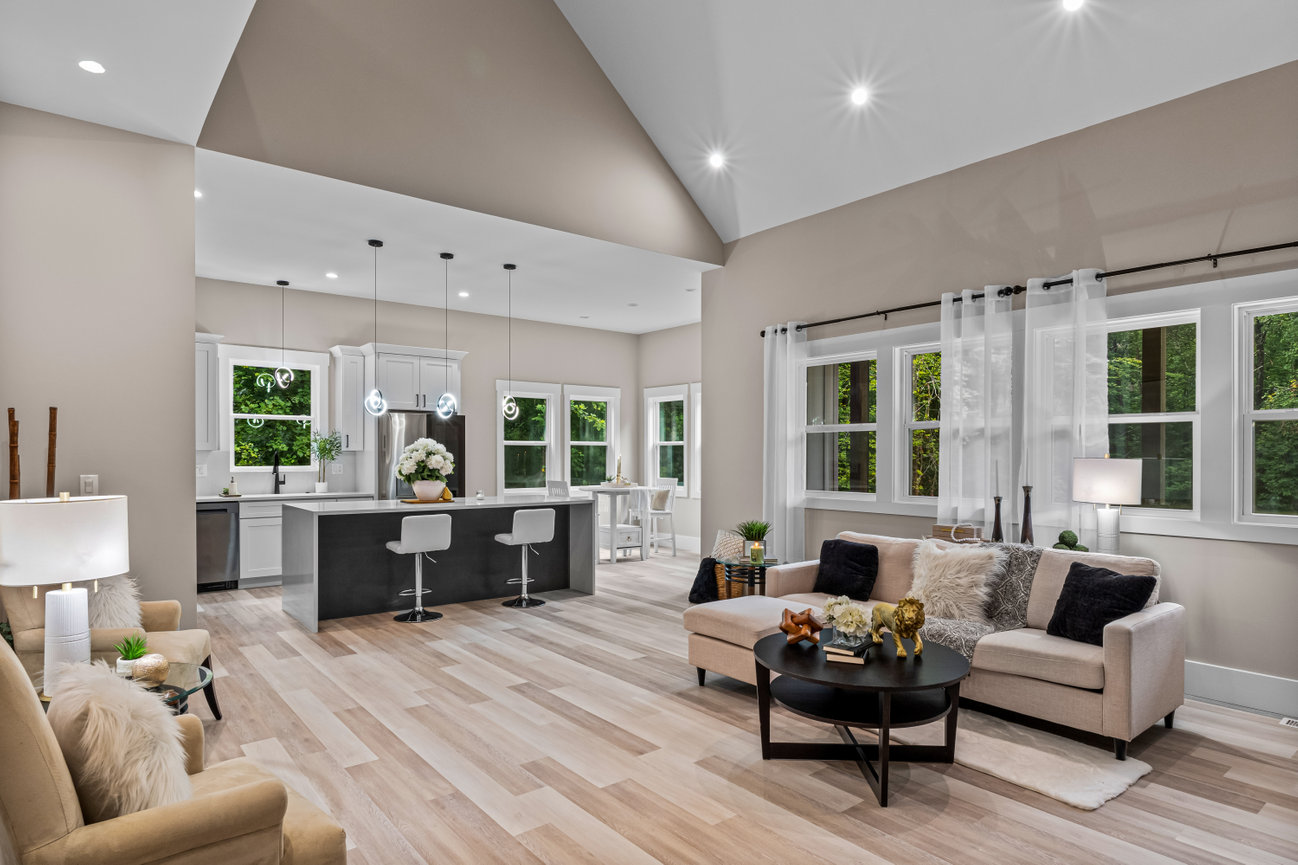 Modern open-concept living room and kitchen with vaulted ceiling, large windows, and light neutral decor