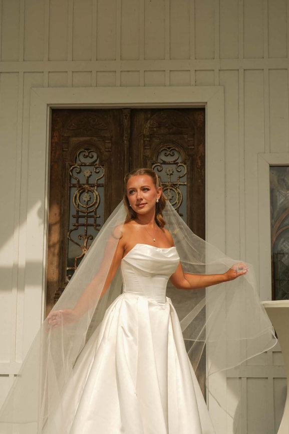 Bride posing with her veil and bouquet beside a decorative doorway.