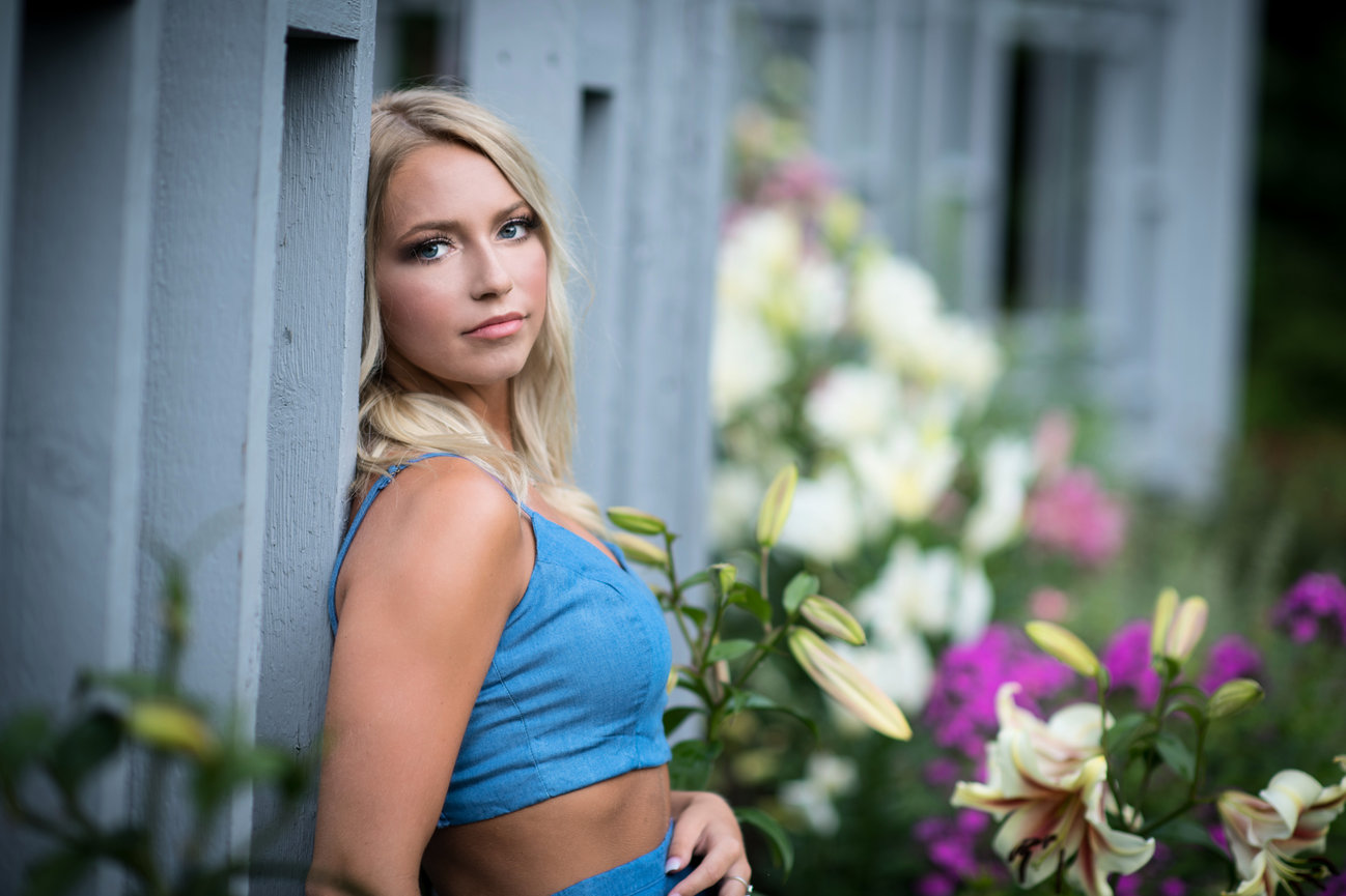 Senior girl with a serious expression leaning against a wooden structure in the center of a rose garden