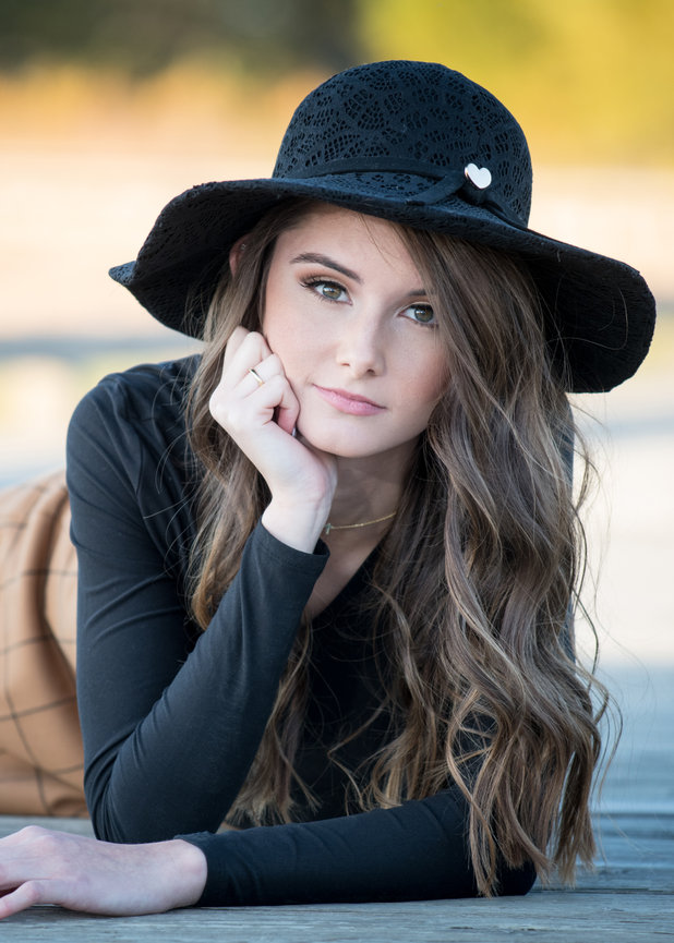 Teenage girl with brown hair laying on a rustic bridge with a black sun hat for senior pictures in Dublin OH.