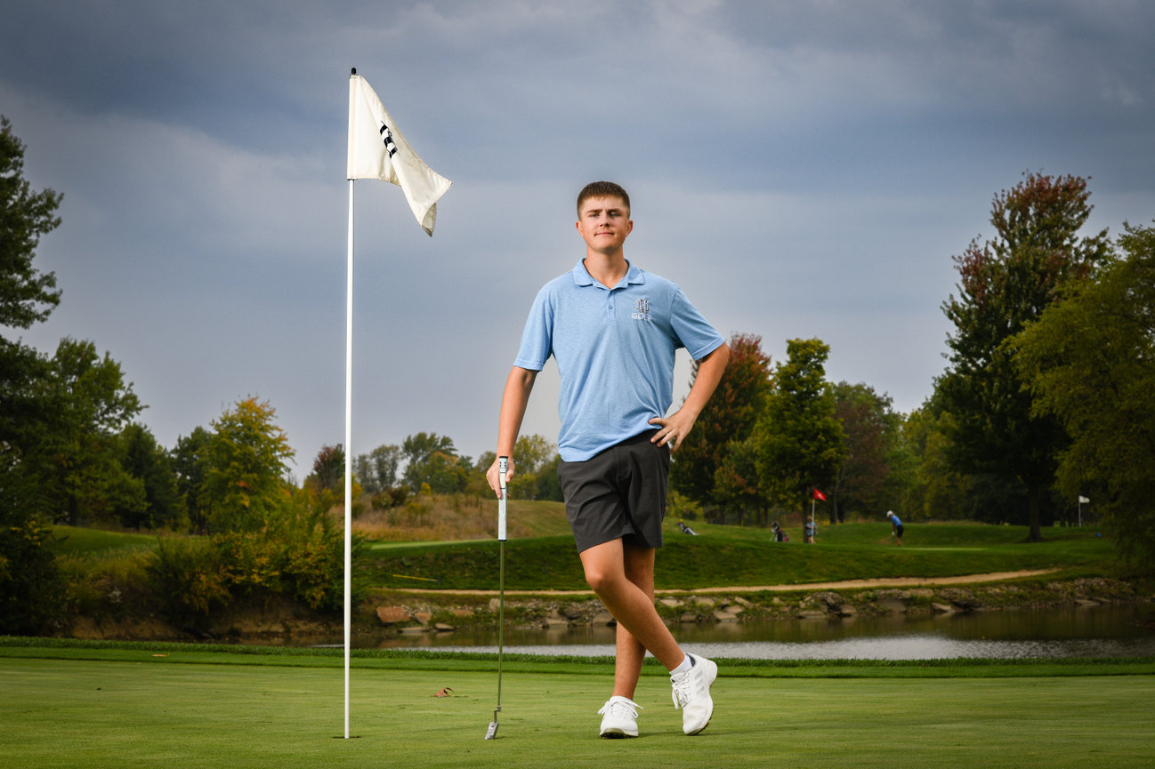 Teenage boy on a golf course in a blue polo and shorts posing for his senior pictures in Dublin OH.