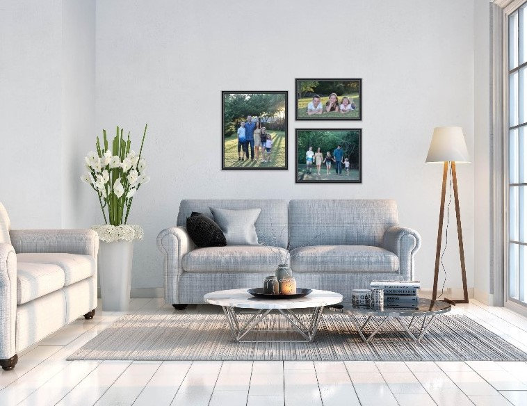 Living room with gray sofas, a floor lamp, a round coffee table, and family wall art. Large window and plant to the side.